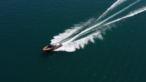Luxury boat in dark color, fast movement on blue water, aerial view. Expensive luxury Italian boat moving on the water top view. Boat dark wood, movement on the water top view.