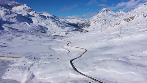 Aerial drone footage of the snow covered Bernina pass road leading to Pontresina along the frozen white lake in winter in Canton Graubunden in the alps in Switzerland