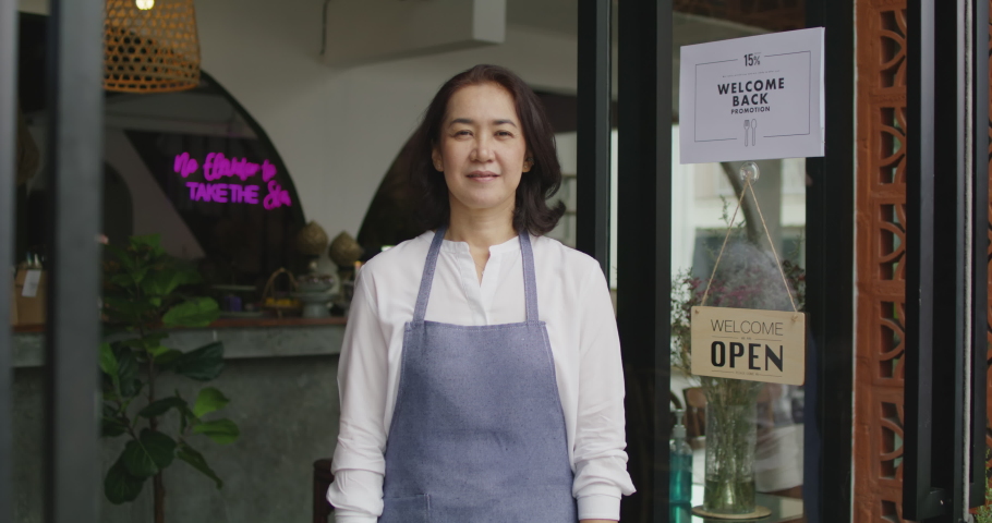 Mature female adult asia people open small bar pub look at camera enjoy laugh work with pride stand at modern SME store. Casual apron chef clerk staff in food or drink cafe coffee shop after pandemic. Royalty-Free Stock Footage #1083848635