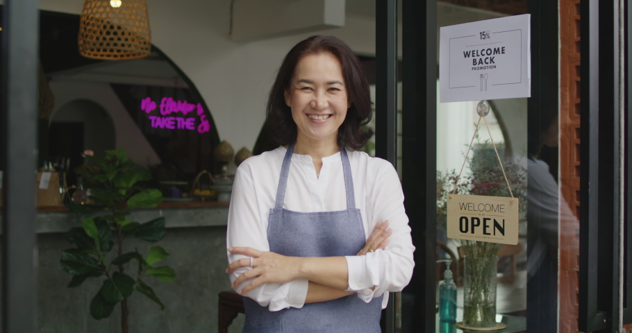 Mature female adult asia people open small bar pub look at camera enjoy laugh work with pride stand at modern SME store. Casual apron chef clerk staff in food or drink cafe coffee shop after pandemic. | Shutterstock HD Video #1083848635