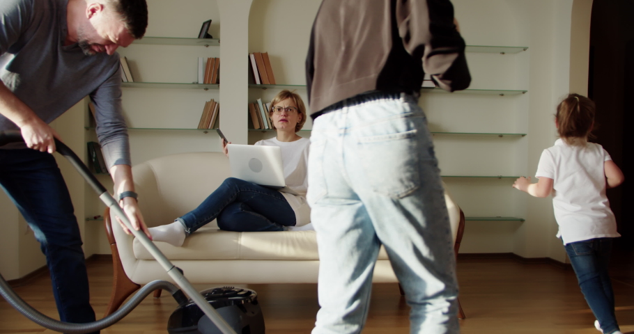Tired wife sitting on the couch, annoyed while a noisy little daughter screams, jumps on the couch and husband does the cleaning in the room. Slow motion | Shutterstock HD Video #1083850654