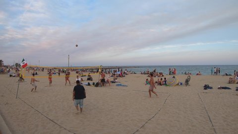 BARCELONA, SPAIN - JULY 2021: Sundown view of Playa de Bogatell, famous beach of Barcelona, Spain. Spanish people swimming, tourists relaxing and playing beach volley on summer holidays at dusk