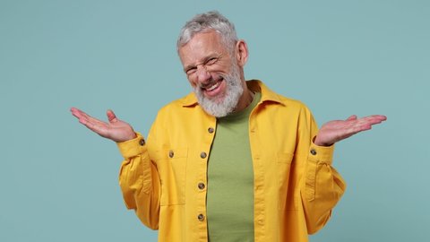 Fun confused shamed elderly gray-haired bearded man 50s wears yellow shirt look camera spreading hands say oops ouch oh omg i am so sorry isolated on plain pastel light blue background studio portrait