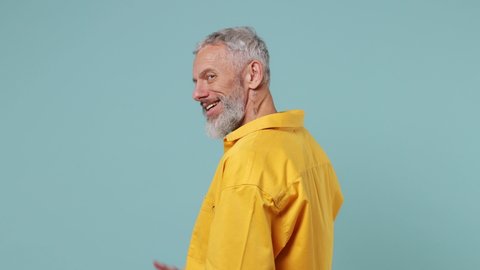 Back rear view excited happy fun elderly gray-haired bearded man 50s wears yellow shirt turn around camera showing thumbs up like gesture isolated on plain pastel light blue background studio portrait