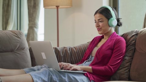 A young attractive Indian Asian female using a laptop to work raises both hands in joy while celebrating the success or completion of the project in an interior house setup. work from home concept