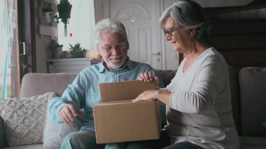 Happy mature aged older family couple unpacking carton box, satisfied with internet store purchase or unexpected gift, feeling excited of fast delivery shipping service, positive shopping experience.
 | Shutterstock HD Video #1083861127