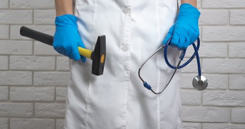 Doctor with hammer. A view of doctor hands in blue latex gloves with a hammer and a stethoscope in the room. Crazy doctor.