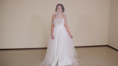 A beautiful young bride in a dress and with a long veil poses in the studio on a white background. Wedding day.