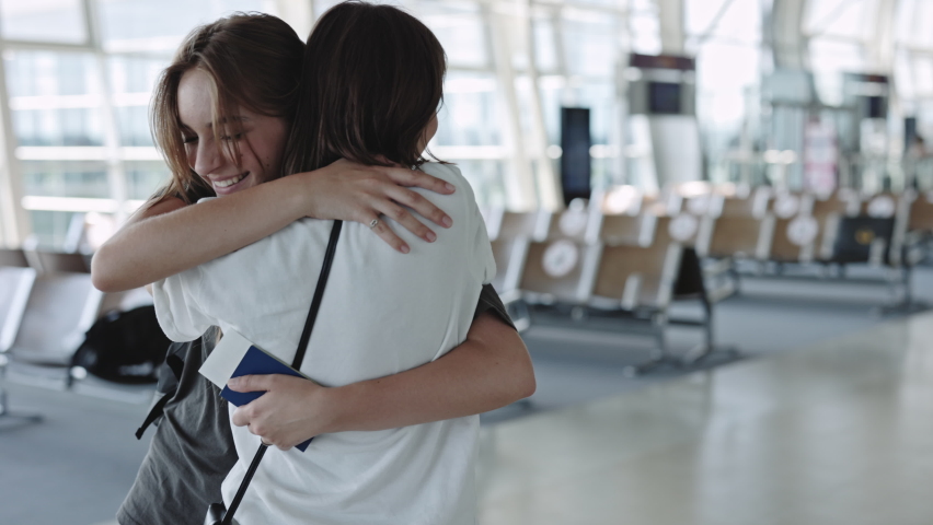 Back view of young woman meeting her loving girlfriend at airport. Two happy lesbians embracing and smiling after departure. Relations and love concept.