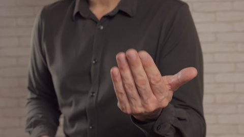 Close-up of a man in dark clothes beckoning with a hand gesture to himself.