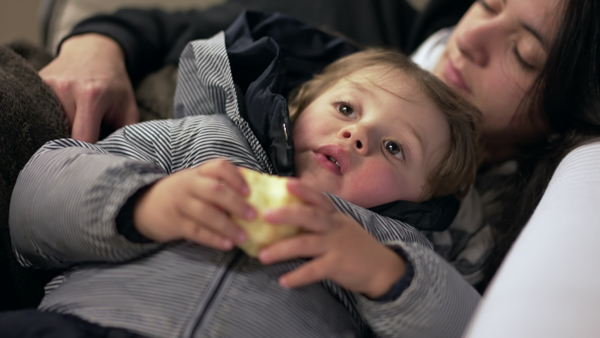 Tired mother napping next to toddler child in sofa couch