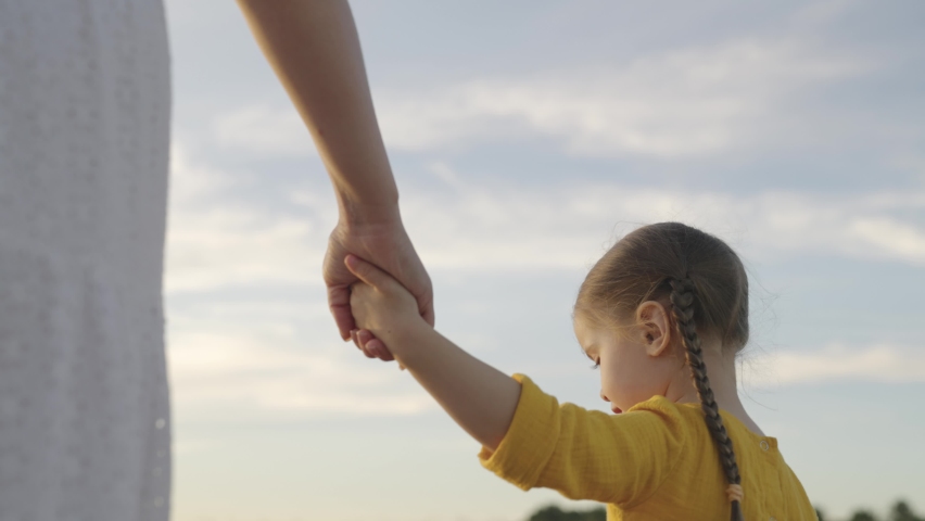 mother leads a small child by the hand against the background of the sky, happy family, kid holds kind mother by hand, baby girl on nature walk, beloved daughter is brought up with parent outdoors Royalty-Free Stock Footage #1083878920