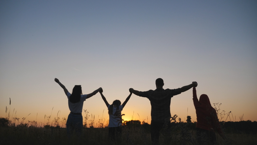Mother and father with two little children stand on grass field with raising hands at sunset. Happy young family enjoy to spending time together at nature. Concept of carefree and freedom. Dolly shot