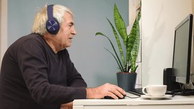 Happy senior man making video call at laptop and waving hand. Old Man with headphones connected with laptop at home. Technology, people, lifestyle and communication concept.