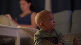 Mother with child in the living room in the evening, cute baby boy is watching tv. High quality 4k footage