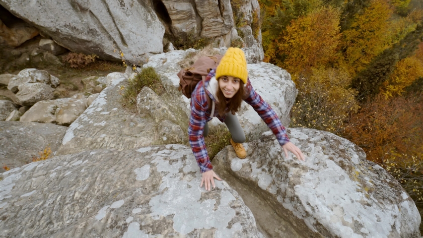 POV first person view of man stretching help hand to pretty woman hiker in yellow beanie with backpack climbing on edge of cliff against background of autumn forest below. girl gives high five on top Royalty-Free Stock Footage #1083887095