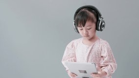 Little Asian girl with headphone enjoy watching video online on tablet and dancing happily.