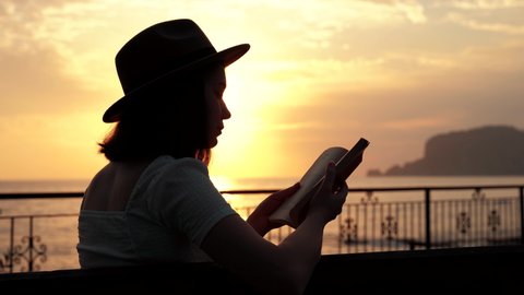 Silhouette of beautiful woman takes zen and reading book in golden lights on beach by coast . summer vacation concept . 4k footage