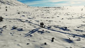 Aerial view of the snowy mountainside, South Ural. Tourists are standing on trail in snow-covered meadow at the foot of the mountain. The blue sky is covered with white clouds. Sunny. Hiking