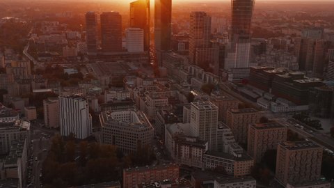 Fly above large city. Tilt up reveal downtown skyscrapers against bright sunset light. Warsaw, Poland