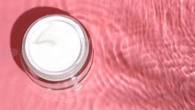 White facial cream on pink background with water ripples and splashes on surface