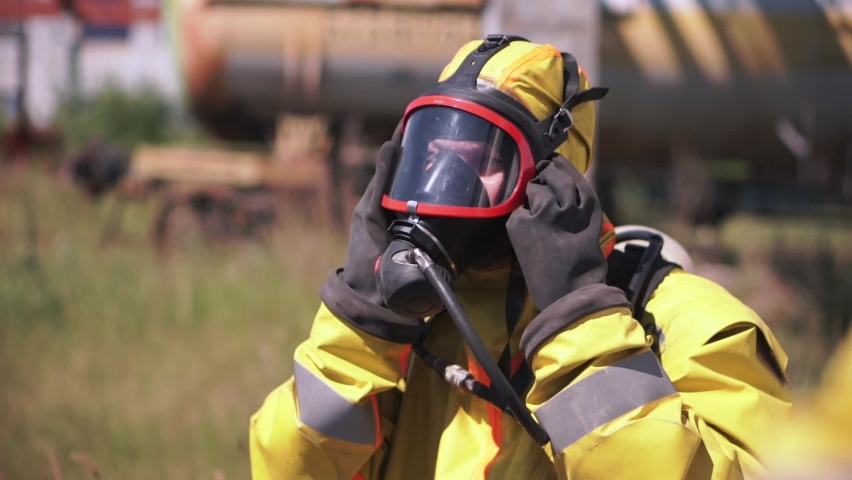Man adjusting a gas mask. Clip. An employee who is wearing a gas mask and a yellow suit is an outdoor worker who is walking from behind Royalty-Free Stock Footage #1083898810