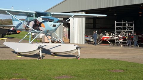 Goodwood, West Sussex, UK, December 10, 2021 . A Cessna 182R Skylane Float plane registered G=ESSL on the apron with people working in the hanger at Goodwood Aerodrome.
