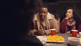 Black adult male chatting to his diverse group of friends around a table at a rooftop party in the nighttime - Powered by Shutterstock - Get 15% off with code: PIKWIZARD15