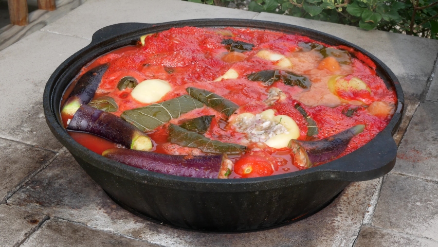 Large caldron with stuffed vegetables in tomato sauce on open fire. Cooking dinner outdoors | Shutterstock HD Video #1083906733