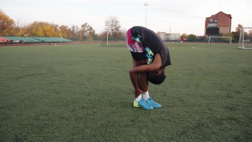 Young black girl working out at the city stadium and doing static stretching exercises with her head pressed to her knees