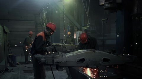 Factory workers in protective helmets and glasses are welding steel and iron part, making the surface smooth. The grinding wheel contacts the detail.Sparks.Metallurgy.Beautiful Epic Shot, Slow motion
