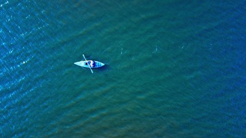 Recreational Kayaking on a lake during a sunset as person paddles into the sunset reflective blue green waters with an aerial drone Birds eye view of steady strokes as the is wearing a life jacket