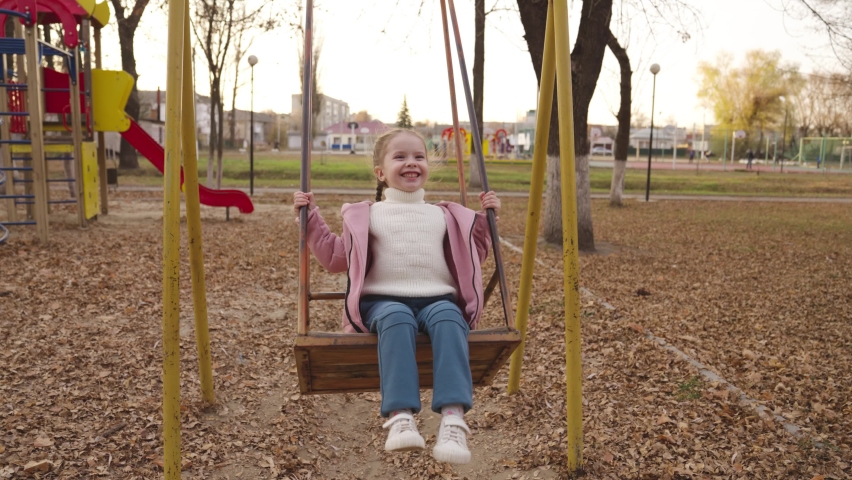 A little cheerful child swinging on a swing in an autumn park, a happy family, a kid soars high in the air, playing a game outdoors on playground, baby girl walks in the park and smiles, children joy Royalty-Free Stock Footage #1083916537