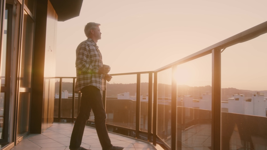 Beautiful morning. Bearded caucasian man walking on balcony terrace, drinking hot coffee and enjoying the scenery. Businessman. Casual lifestyle.