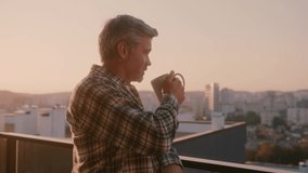 Bearded casual man with cup of coffee enjoying tranquil peaceful sunny morning on balcony apartment. City life. Beautiful scenery. - Powered by Shutterstock - Get 15% off with code: PIKWIZARD15
