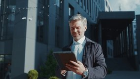 Close up handsome businessman using his tablet computer - scrolling, taping and texting walking near office. Smiling. Feel happy. Outdoor sunlight. Slow motion - Powered by Shutterstock - Get 15% off with code: PIKWIZARD15