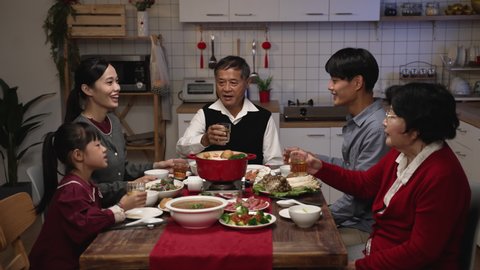 cheerful chinese family with mixed generation raising glasses to toast new year as they are gathering to have reunion dinner in celebration of spring festival at home