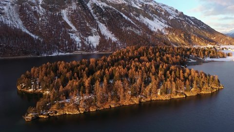 Aerial drone footage of the sunset over the Silsersee lake in winter in the Engadine valley in Sils Maria village in Canton Graubunden in the Swiss alps. Shot with a rotation motion