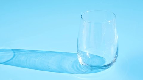 Milk is poured into a glass transparent glass on blue background close up.
