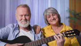 portrait of senior male and female retirees having fun playing guitar and singing while sitting on couch at home, smiling and looking at the camera - Powered by Shutterstock - Get 15% off with code: PIKWIZARD15