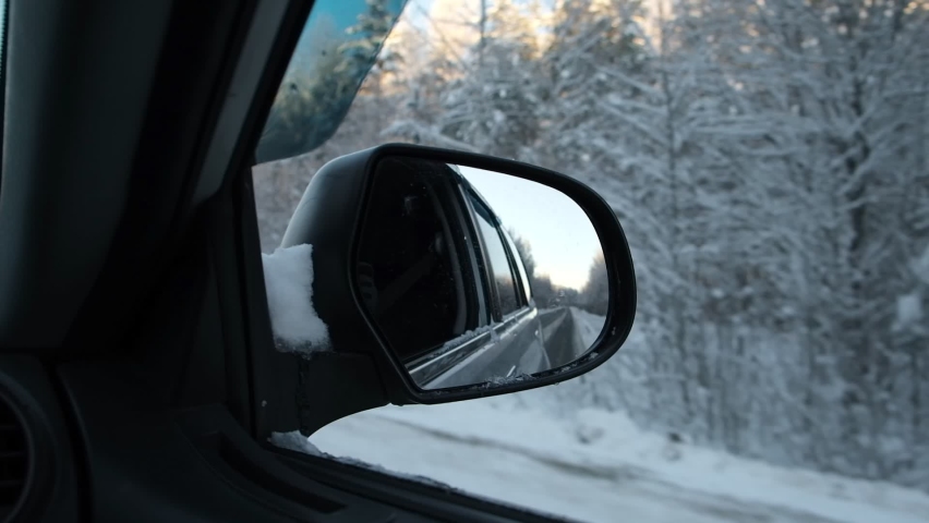 Side view mirror reflection of winter forest road. Landscape with empty highway going through the Snowy forest. Car speeding on road. Auto in motion. Tourism, travel, trip concept. Snow covered trees.