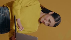 Vertical video: Young adult typing on laptop pc with technology in studio. Asian woman using portable computer to browse internet, advertising freelance work and modern communication on device.
