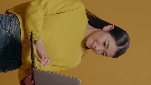 Vertical video: Young adult typing on laptop pc with technology in studio. Asian woman using portable computer to browse internet, advertising freelance work and modern communication on device.