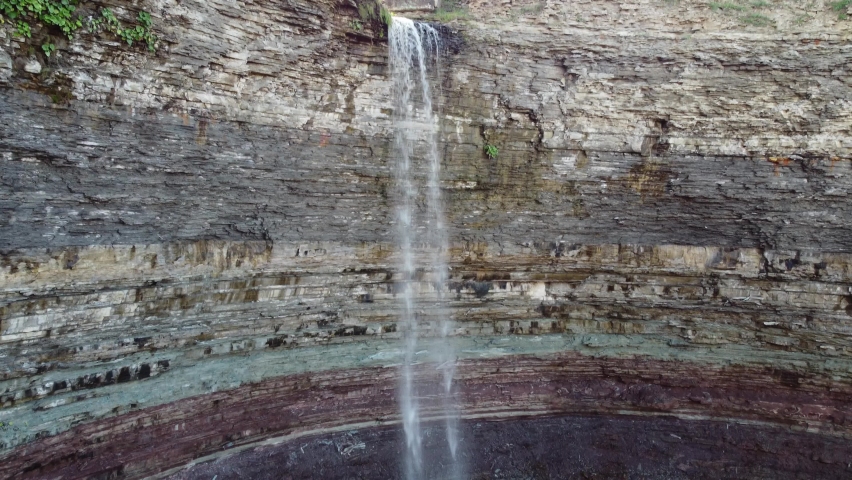 Spectacular scenic view of famous Devil’s Punchbowl, rock formation with waterfall pouring down to the bottom located at Hamilton, Ontario Canada, slow aerial pedestal down shot.