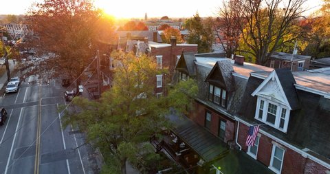 American flag hangs from city home in USA. Gorgeous light at golden hour. Pride in America. Establishing aerial shot quiet peaceful town.