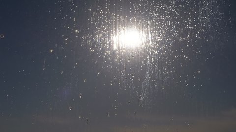 Raindrops Run Down the Glass in the Reflection of the Sunbeams at Sunset. Beautiful sunset through the window in the bright, iridescent glare of the sun rays. Sunshine. Zoom. Close up.