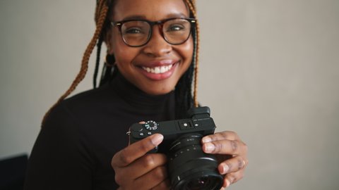 Cheerful female photographer capturing pictures with a dslr camera. Creative young woman smiling happily while using a camera in her home studio.