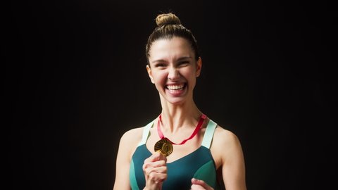 Happy sportswoman winner holding golden medal close-up. Woman athlete standing on black background, having first place. Award and victory, winning the championship. 