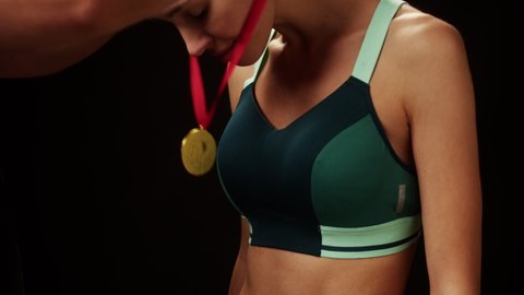 Awarding sportswoman with gold medal close-up. Woman athlete winner standing on black background, having first place. Award and victory, winning the championship. 