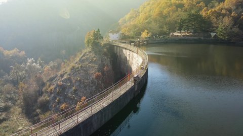 Aerial view of a dam bridge with the lake reflecting the colorful autumn forest in the background